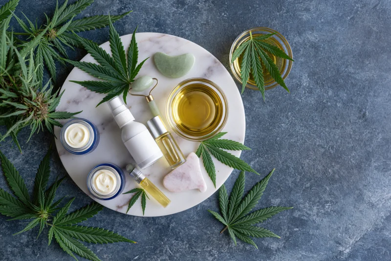 Cbd skincare products arranged on a round marble tray with cannabis leaves and jars of cream and oil