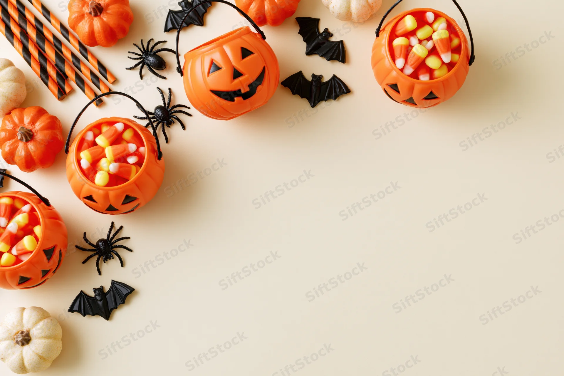 Halloween decorations including pumpkins, bats, spiders, and candy arranged along the left side of a flat surface with copyspace on the right