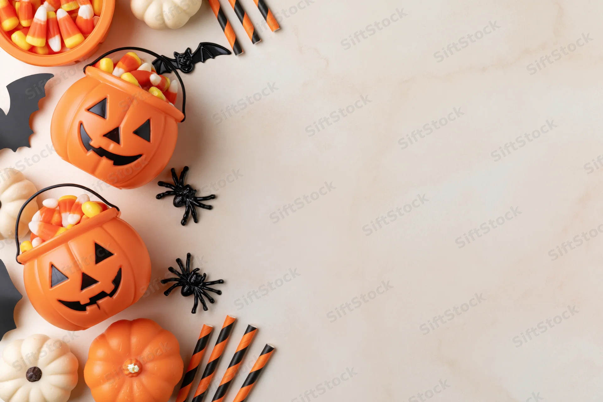 Halloween decorations including pumpkins, candy, spiders and bats arranged along the left side of a marble surface with copyspace on the right