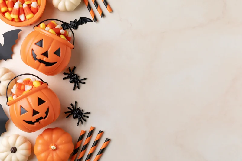 Halloween decorations including pumpkins, candy, spiders and bats arranged along the left side of a marble surface with copyspace on the right