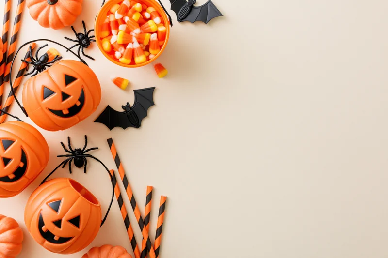 Halloween decorations including pumpkins, bats, spiders, and candy arranged along the left side of a flat surface with copyspace on the right