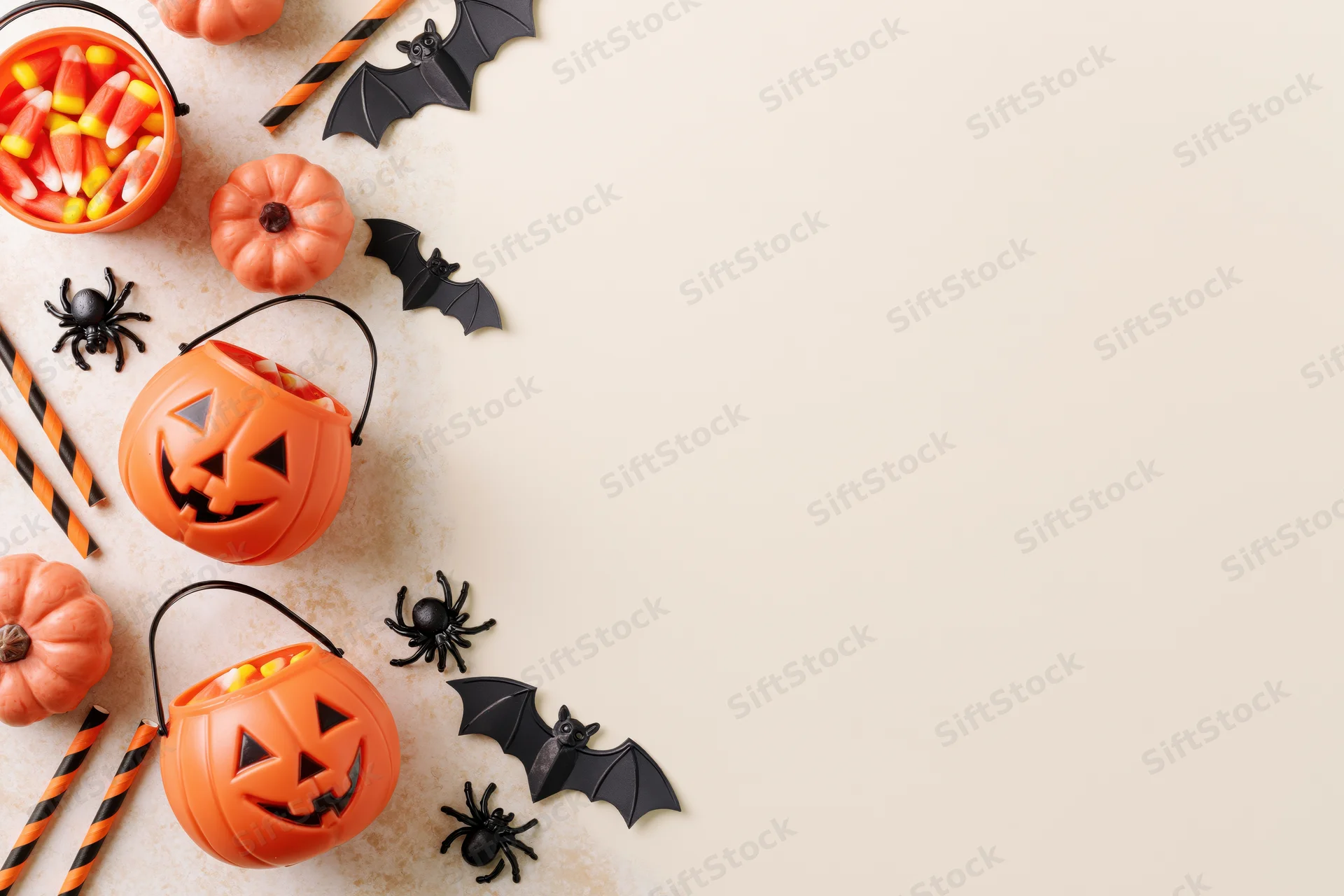 Halloween decorations including pumpkins, bats, spiders, and candy arranged in flat lay on light surface with copyspace on right
