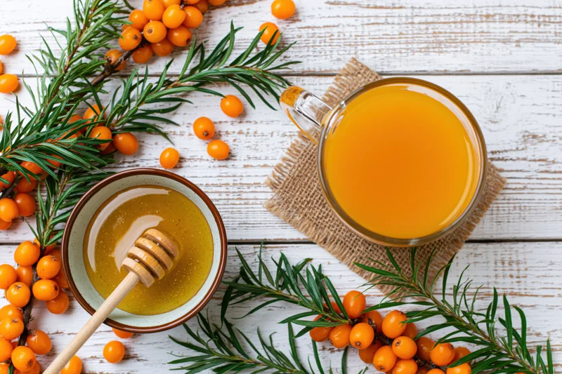 Glass mug of sea buckthorn juice with honey and fresh berries on a white wooden surface