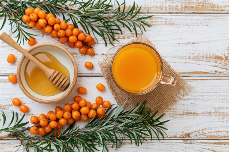 Glass mug of sea buckthorn tea with honey and fresh berries on a white wooden table