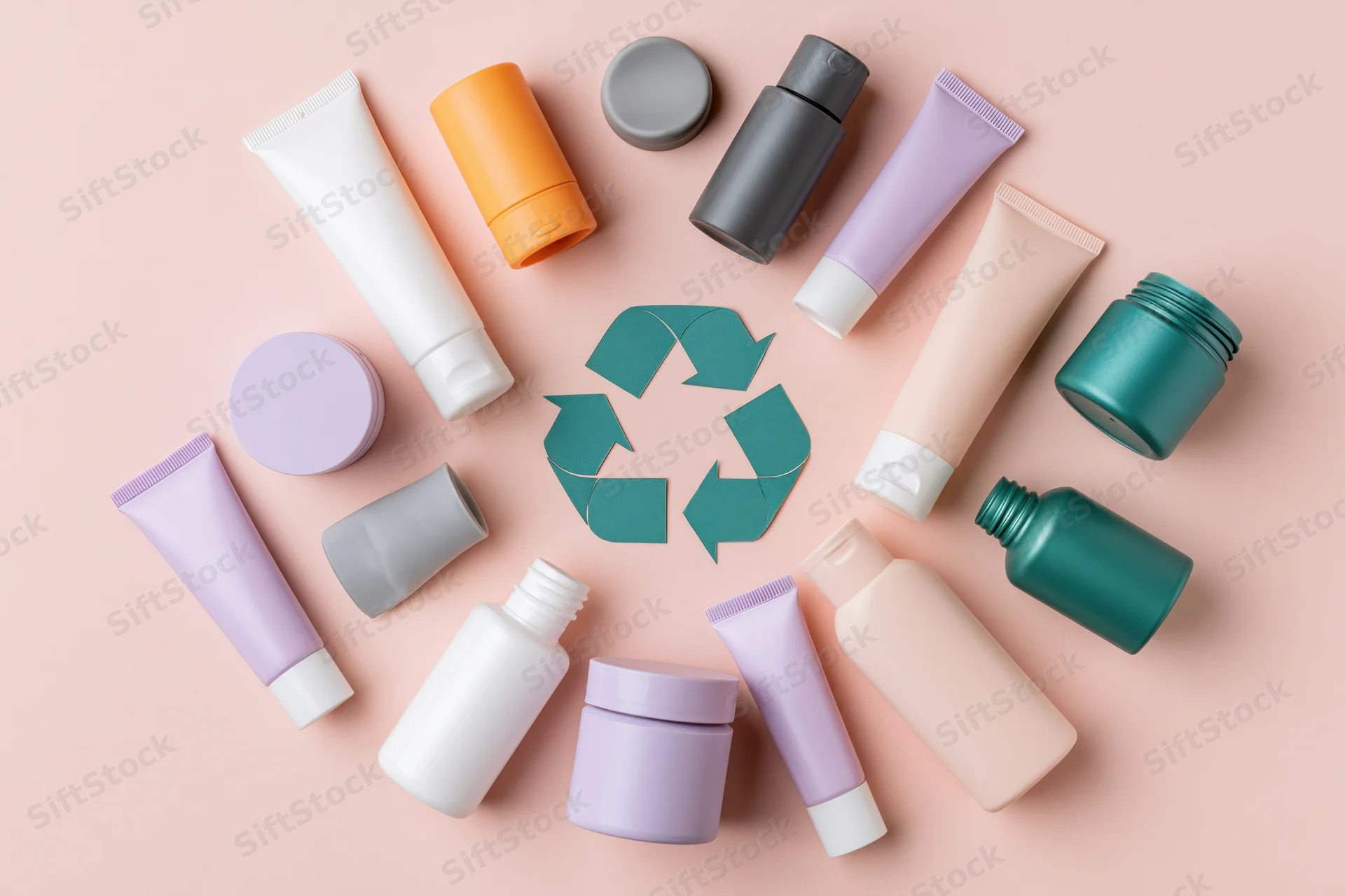 Empty cosmetic plastic containers arranged in circle around recycling symbol on pastel pink background