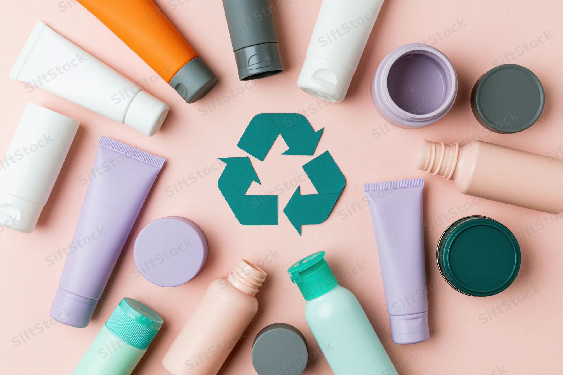 Empty cosmetic plastic containers arranged around a recycling symbol on a pastel pink background