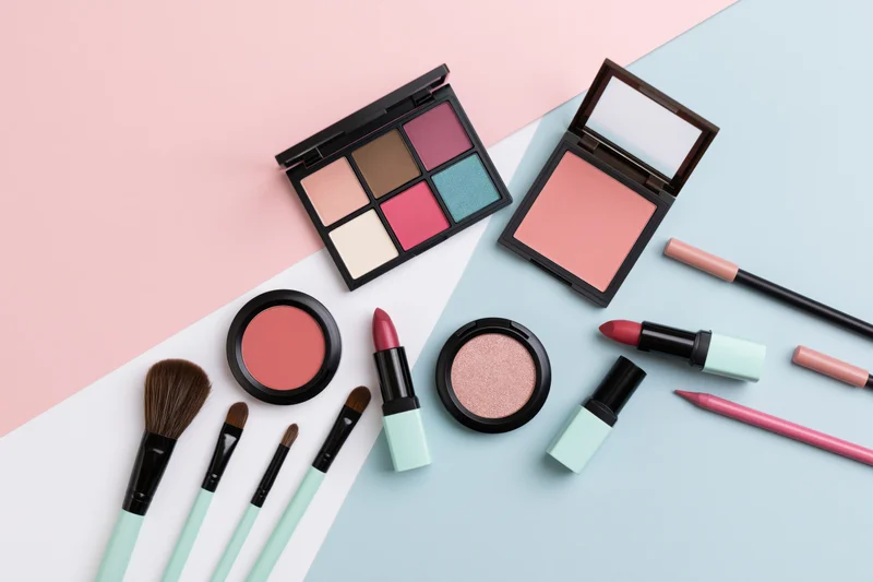 Assorted makeup products arranged in flat lay on pastel background