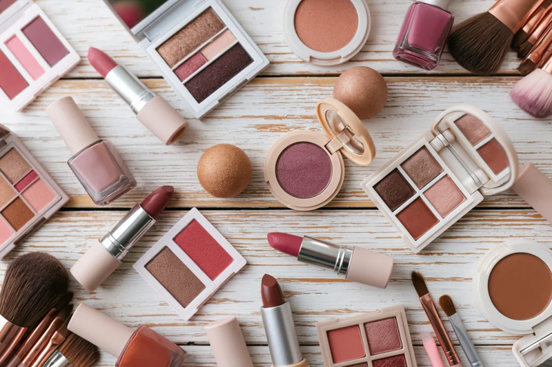 Assorted makeup products arranged in flat lay on white wooden surface