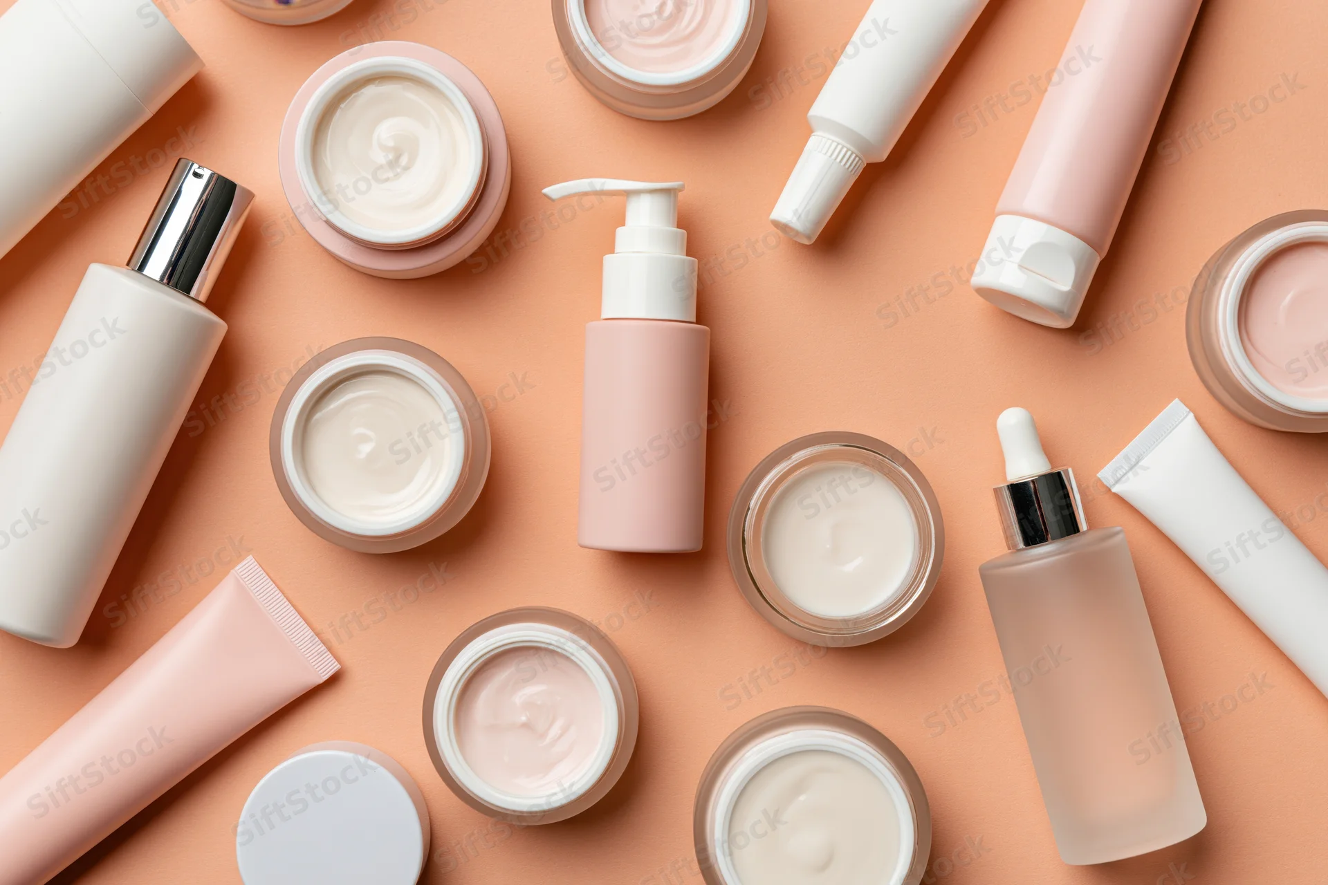 Assorted skincare products arranged in flat lay on peach background