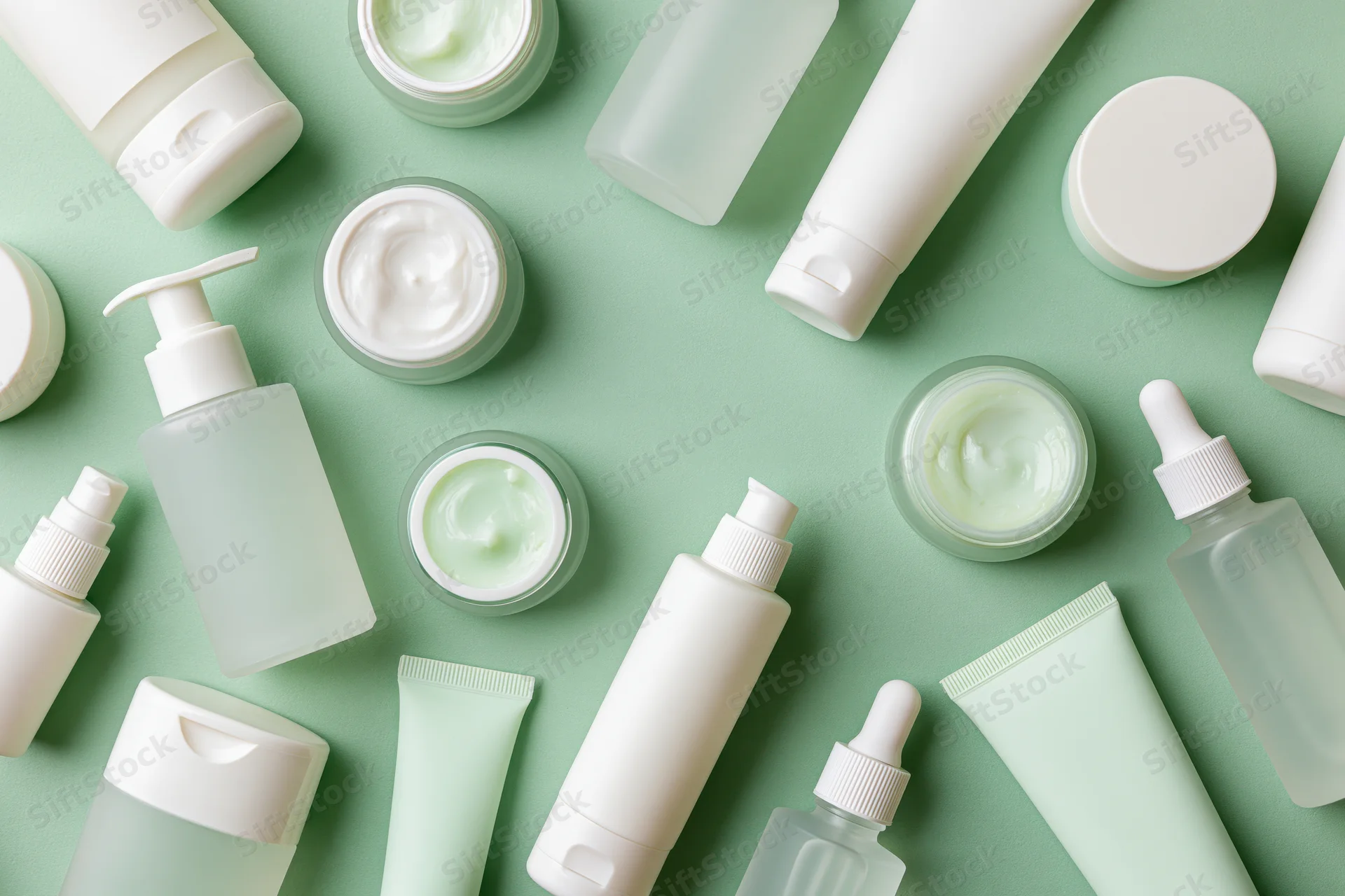 Assorted unlabeled skincare products arranged in flat lay on mint green background