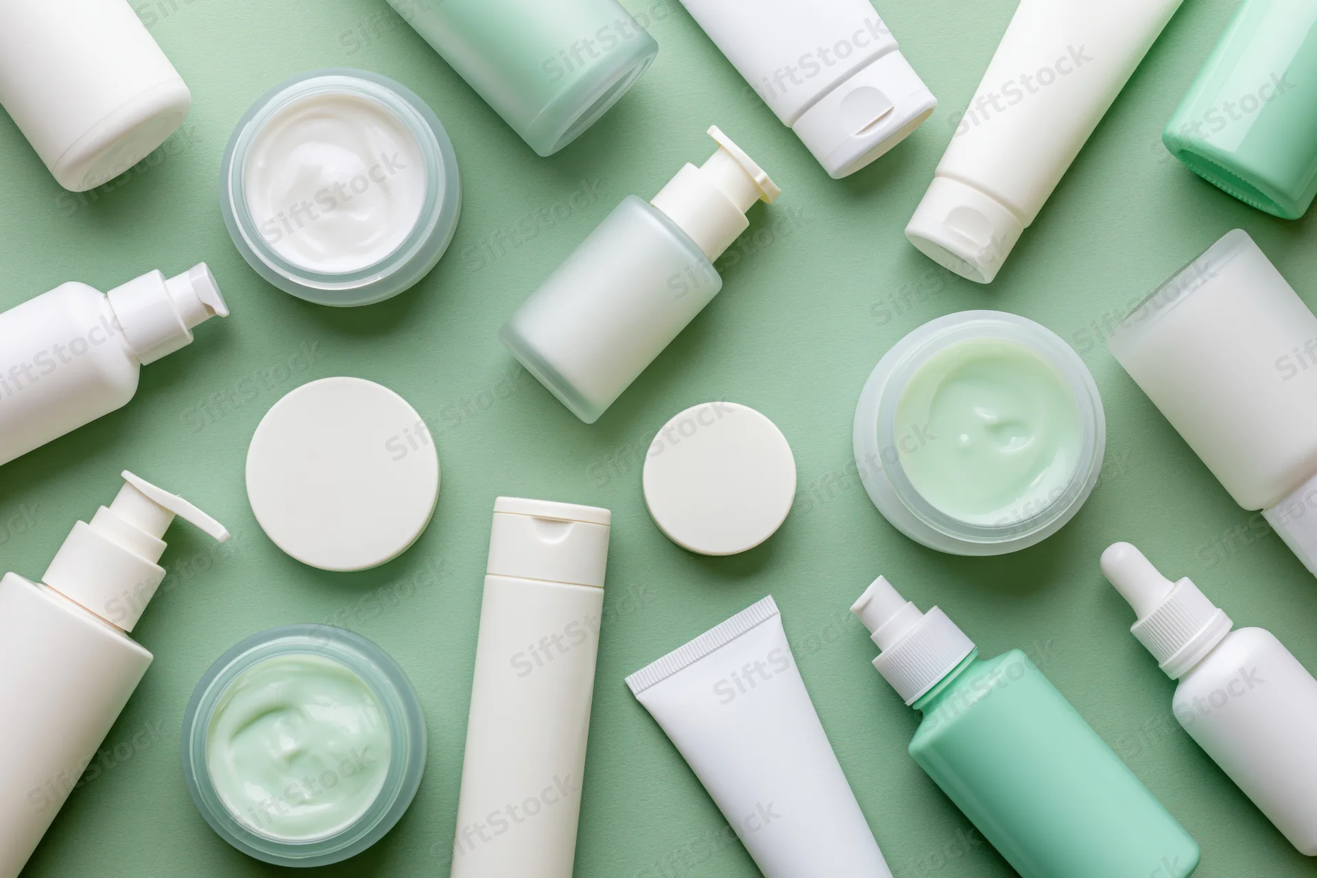 Assorted unlabeled skincare products arranged in flat lay on green background