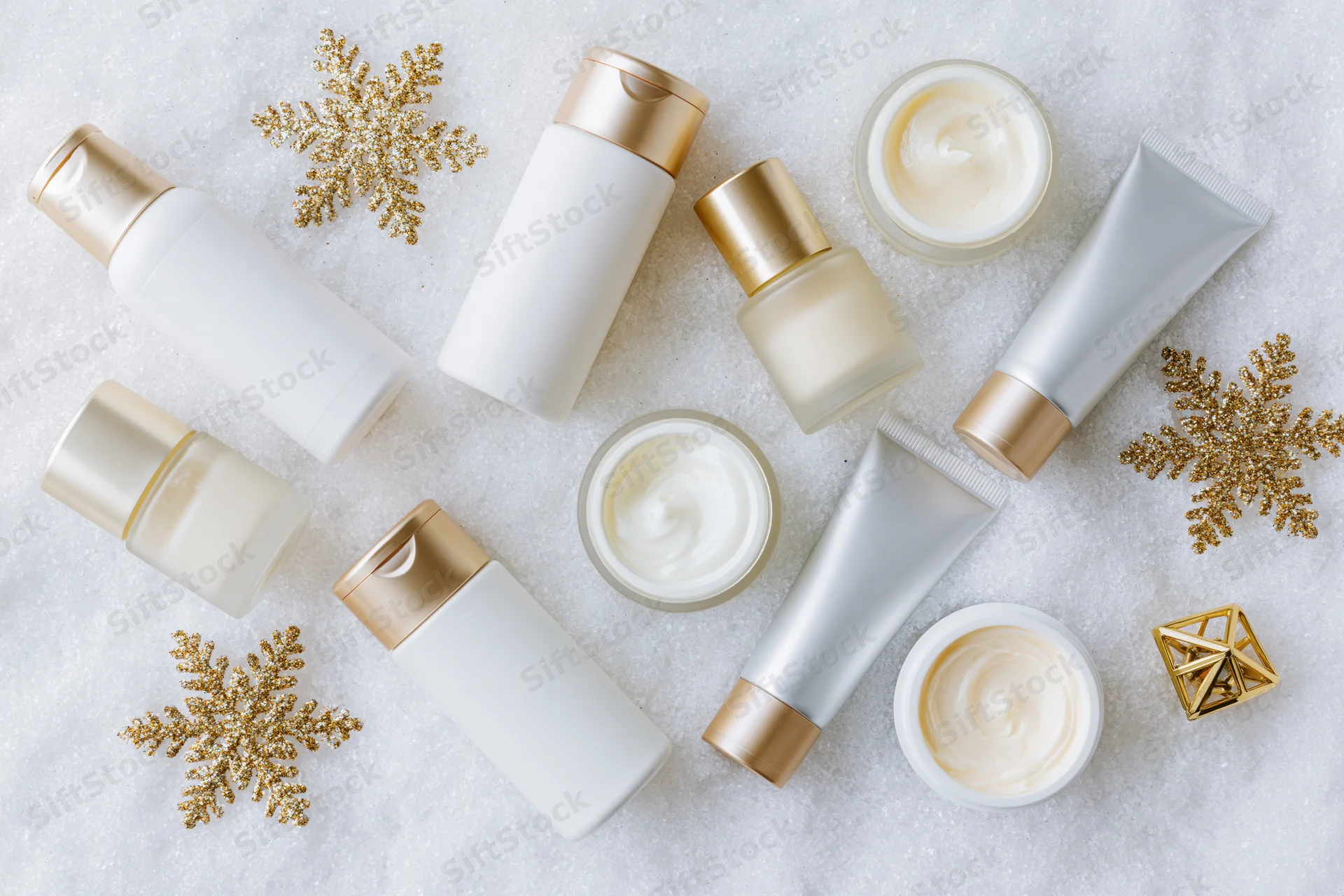 Assorted skincare products with gold snowflakes arranged on snowy surface