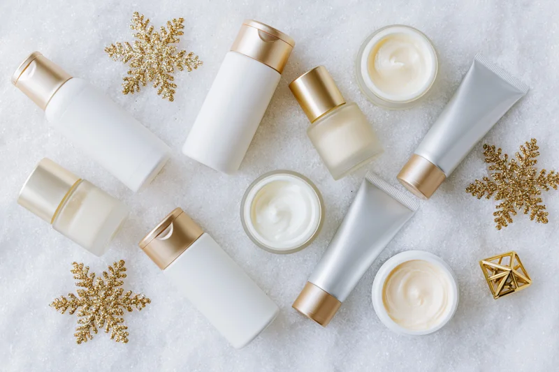 Assorted skincare products with gold snowflakes arranged on snowy surface