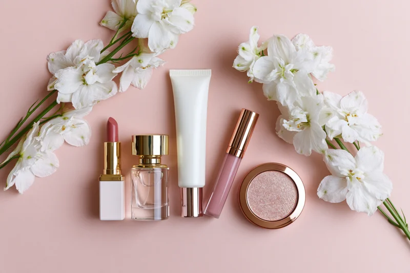 Beauty products arranged with white flowers on a pink surface in a flat lay composition
