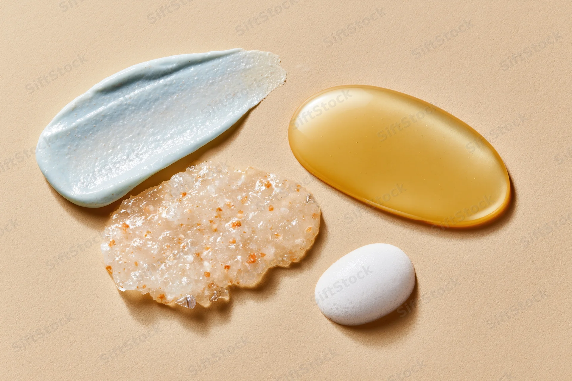 Four skincare product smears arranged on a warm beige surface in a flat lay composition