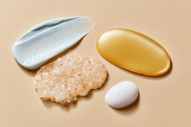 Four skincare product smears arranged on a warm beige surface in a flat lay composition
