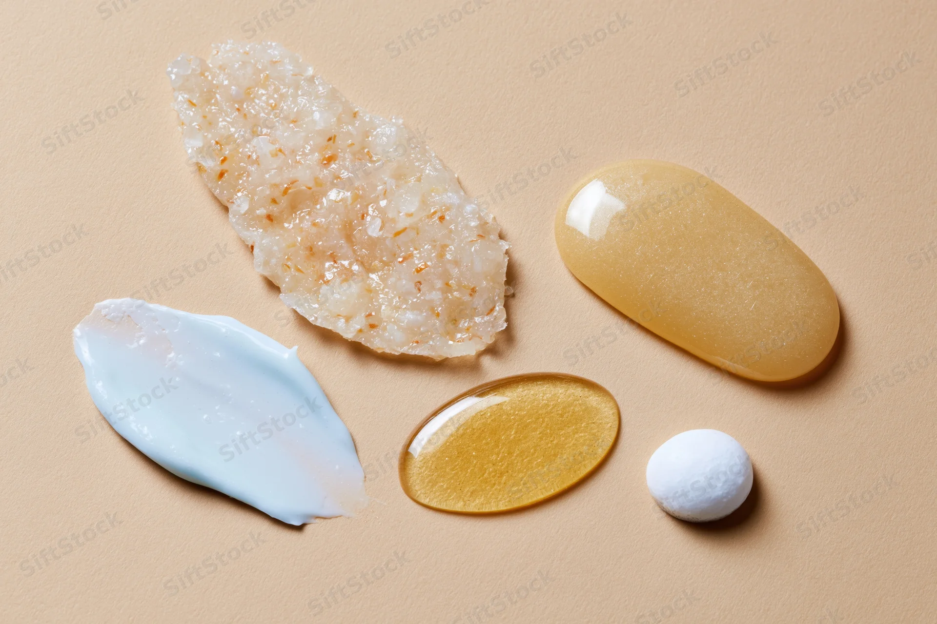 Four skincare product smears arranged on a warm beige surface in flat lay view