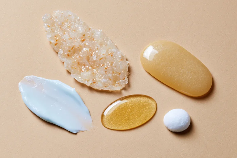 Four skincare product smears arranged on a warm beige surface in flat lay view