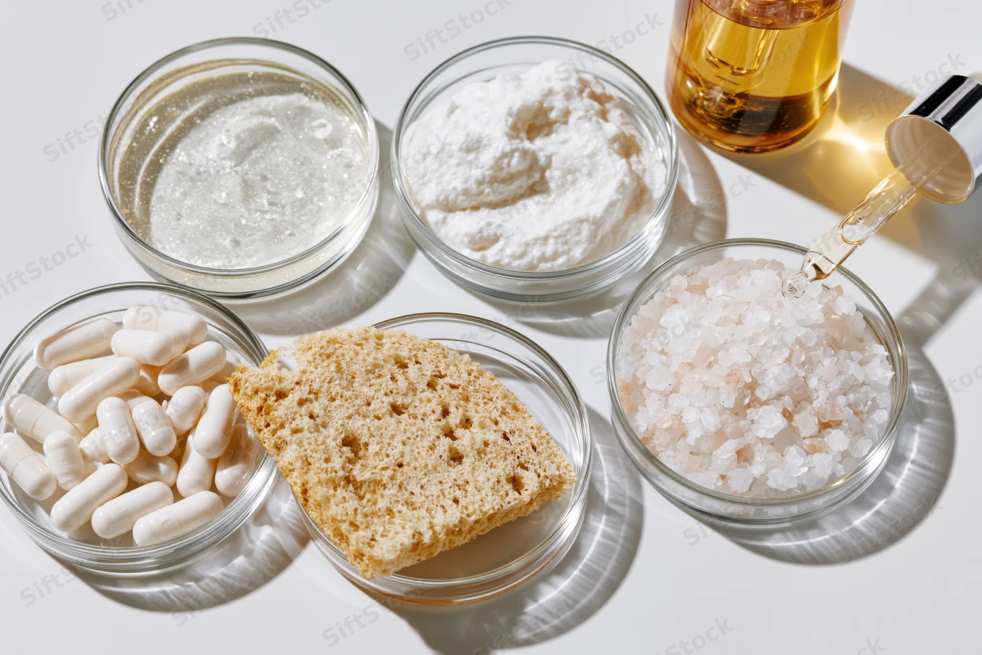 Glass petri dishes holding various supplements and food ingredients arranged on white surface