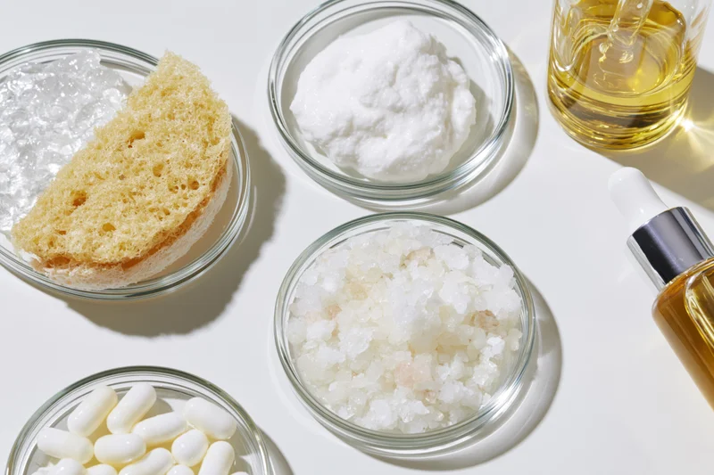 Skincare ingredients arranged in glass bowls on white surface
