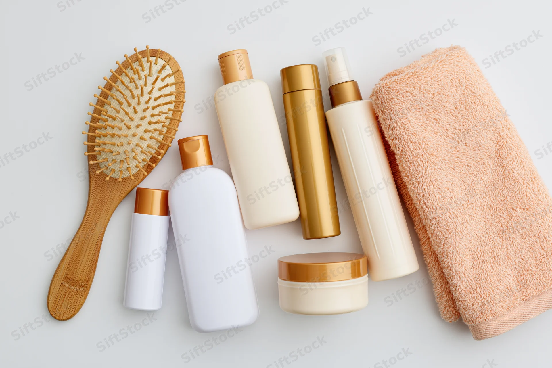 Hair care products arranged in flat lay on white surface with bamboo brush and towel