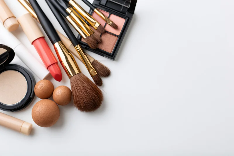 Makeup products arranged in flat lay on white surface with copyspace