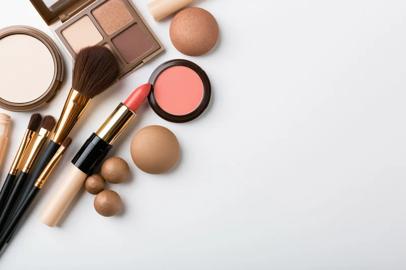 Makeup products arranged in flat lay on white surface with copyspace
