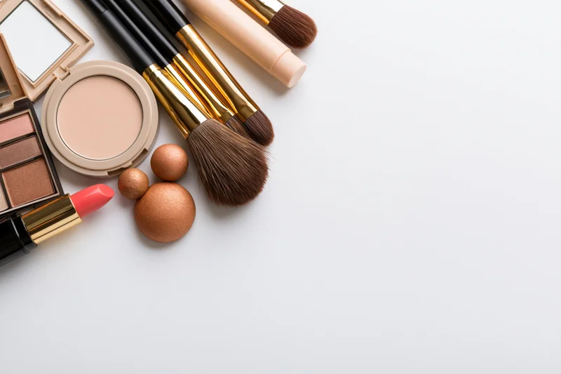 Makeup products arranged in flat lay on white surface with copyspace