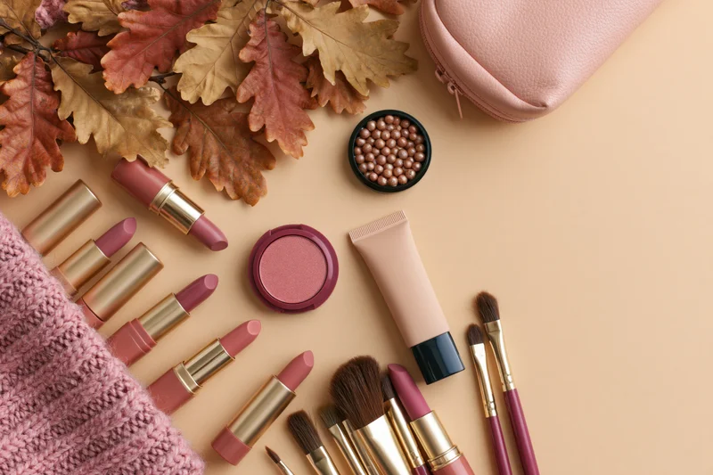 Makeup products arranged with autumn leaves on a warm beige surface