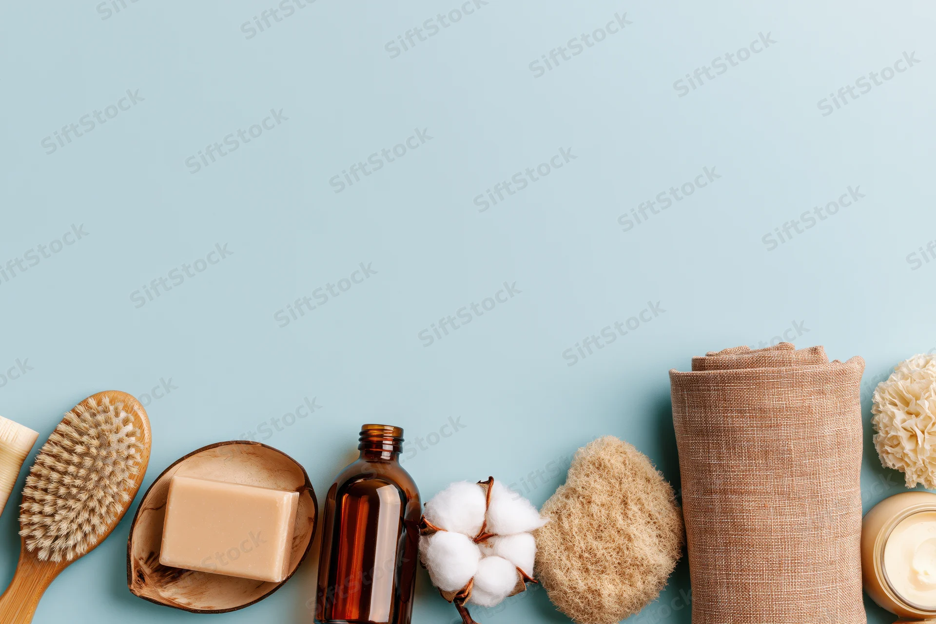 Natural skincare and bathroom products arranged in a flat lay on a light blue background with copyspace
