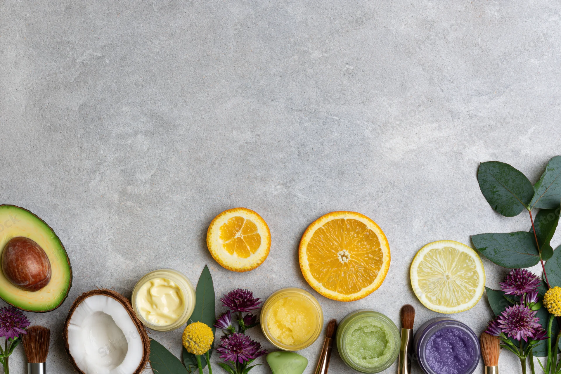 Natural skincare ingredients and products arranged in a flat lay on a gray textured surface with copyspace above