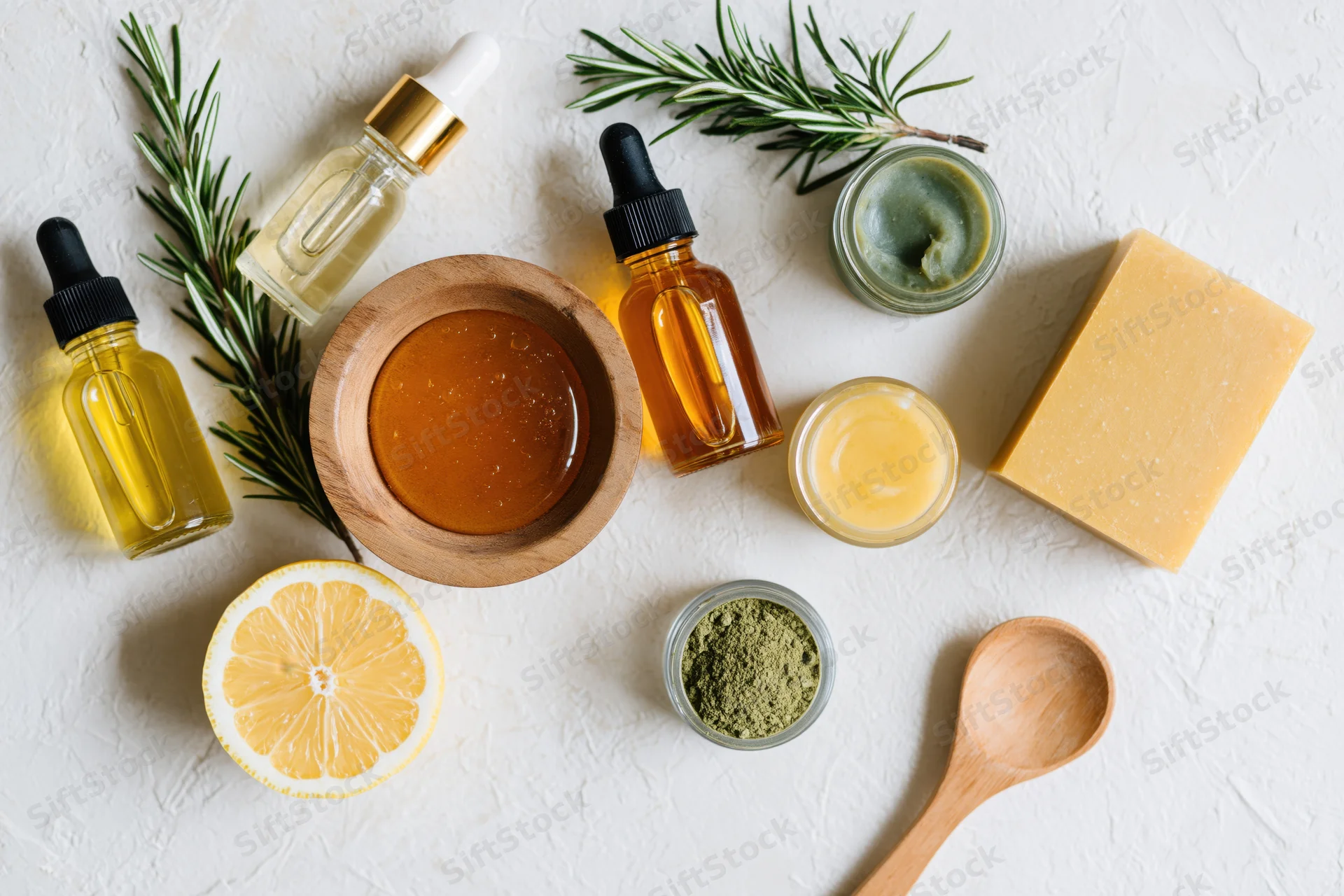 Natural skincare ingredients arranged in flat lay on white surface with rosemary, lemon, honey, soap, and glass bottles