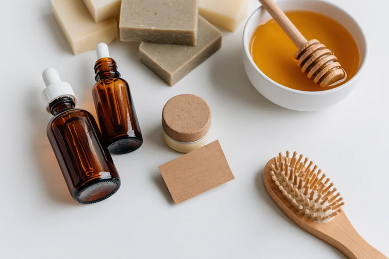 Natural skincare products arranged in flat lay on white surface with honey, soap bars, dropper bottles, and wooden brush