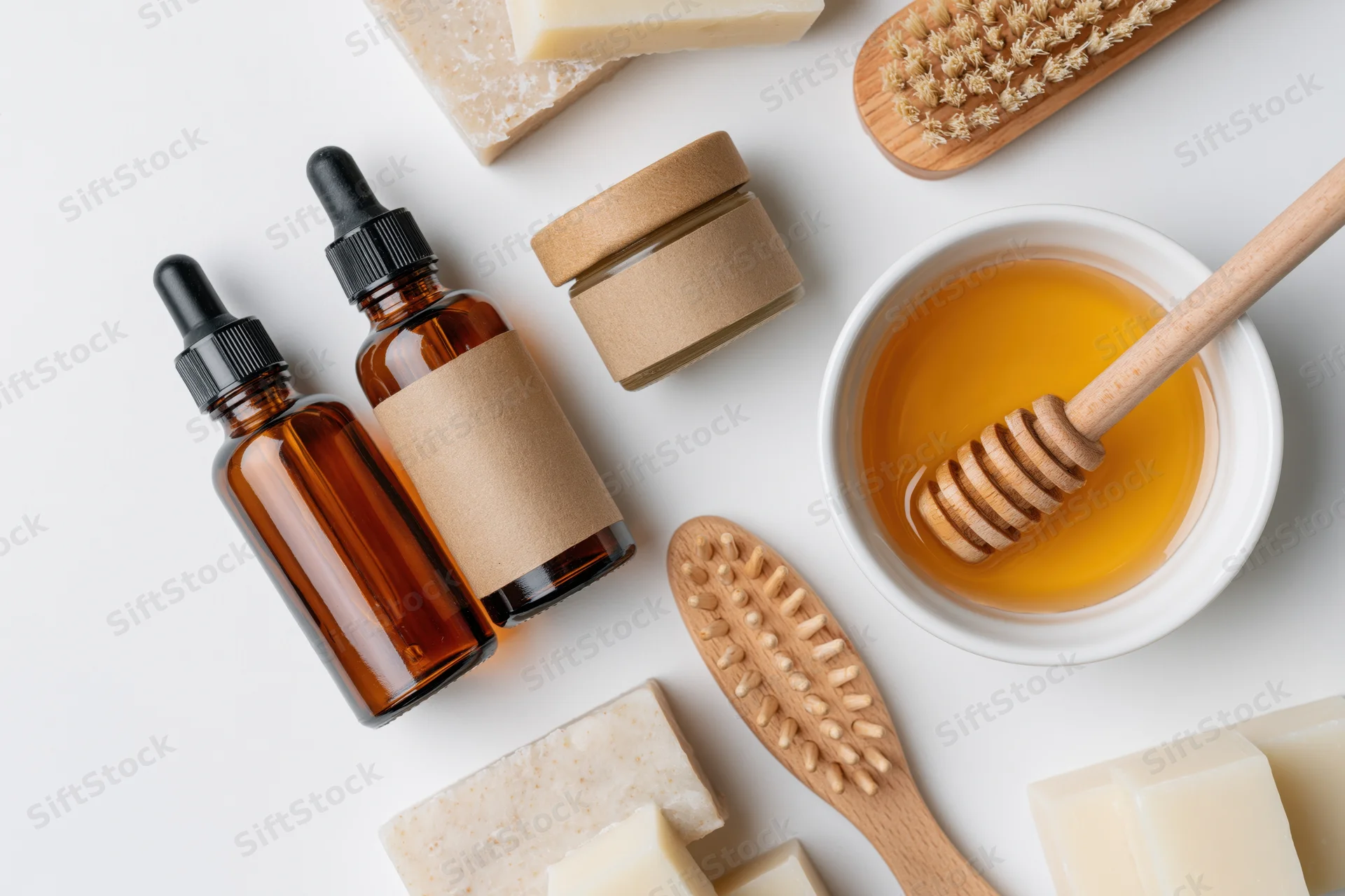 Natural skincare products arranged on white surface with honey, soap, wooden brushes and amber bottles