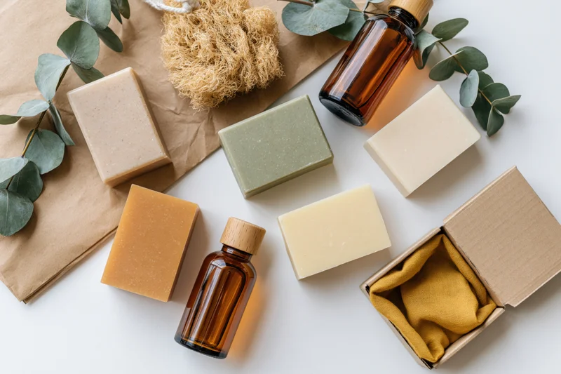 Natural skincare products arranged in flat lay on white surface with eucalyptus leaves and amber bottles
