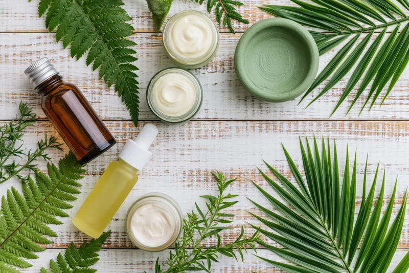 Natural skincare products with cream jars, amber glass bottles and green leaves arranged on a white wooden table