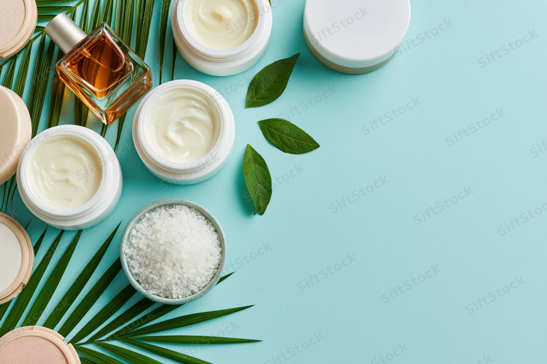 Skincare and beauty products arranged with leaves and salt on a blue surface