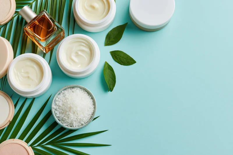 Skincare and beauty products arranged with leaves and salt on a blue surface
