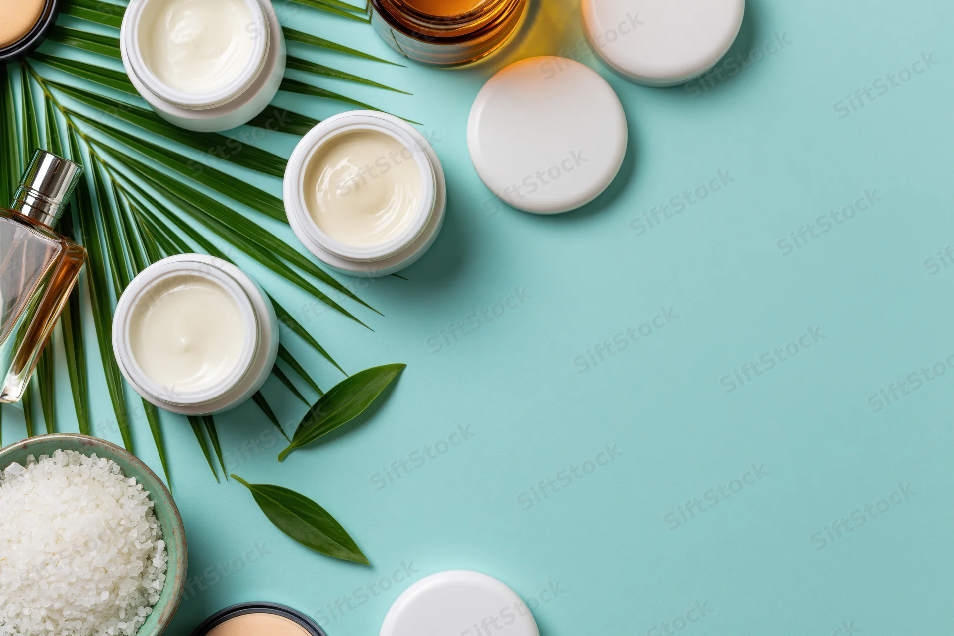 Skincare products and green leaves arranged on teal surface in flat lay composition