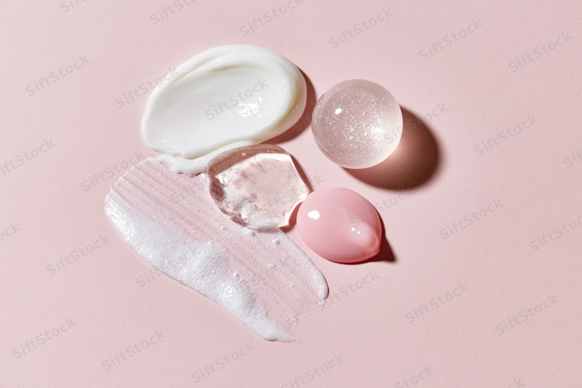 Skincare product swatches and dollops arranged on a pale pink surface in a flat lay composition