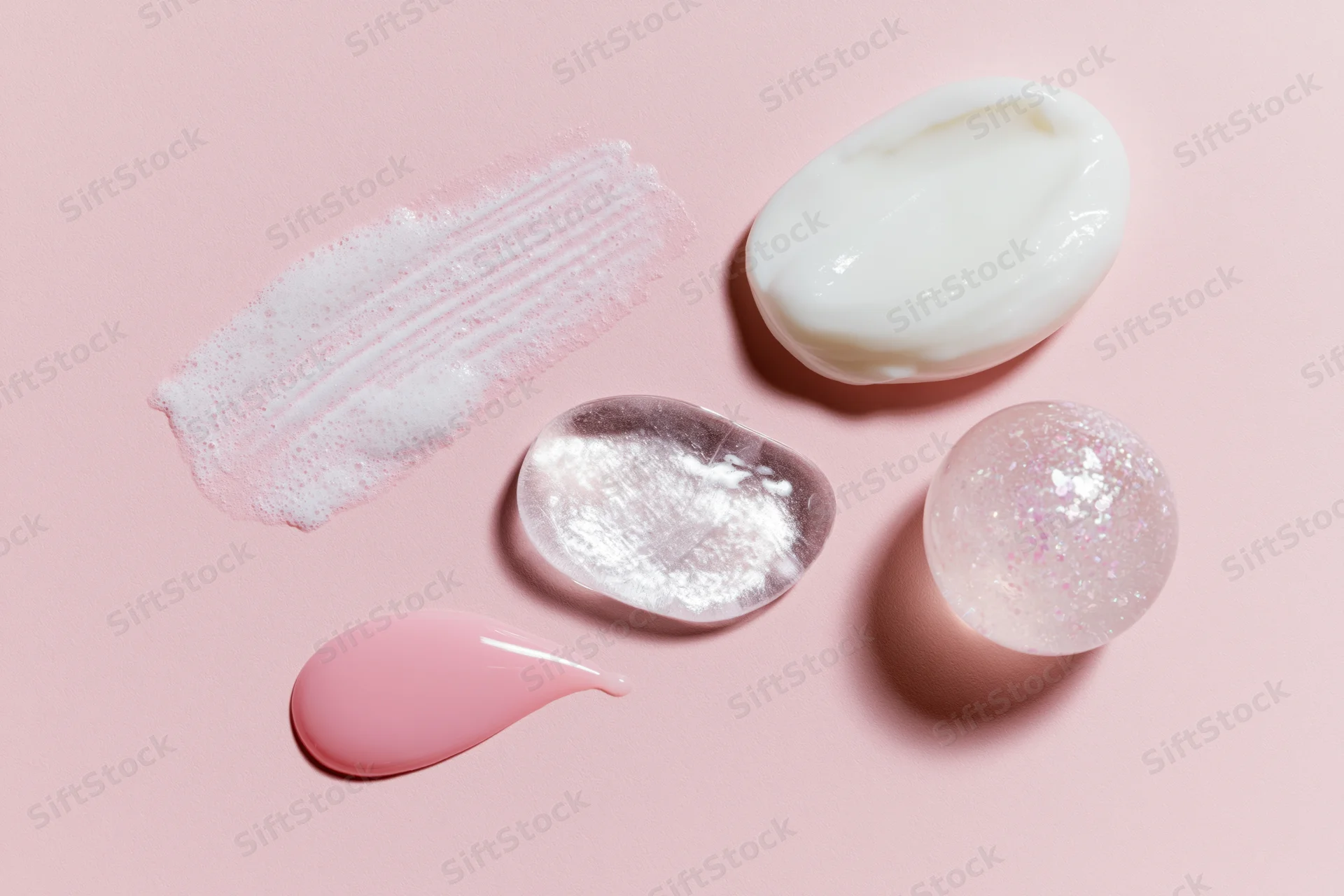 Flat lay of skincare product swatches and dollops on a pale pink background