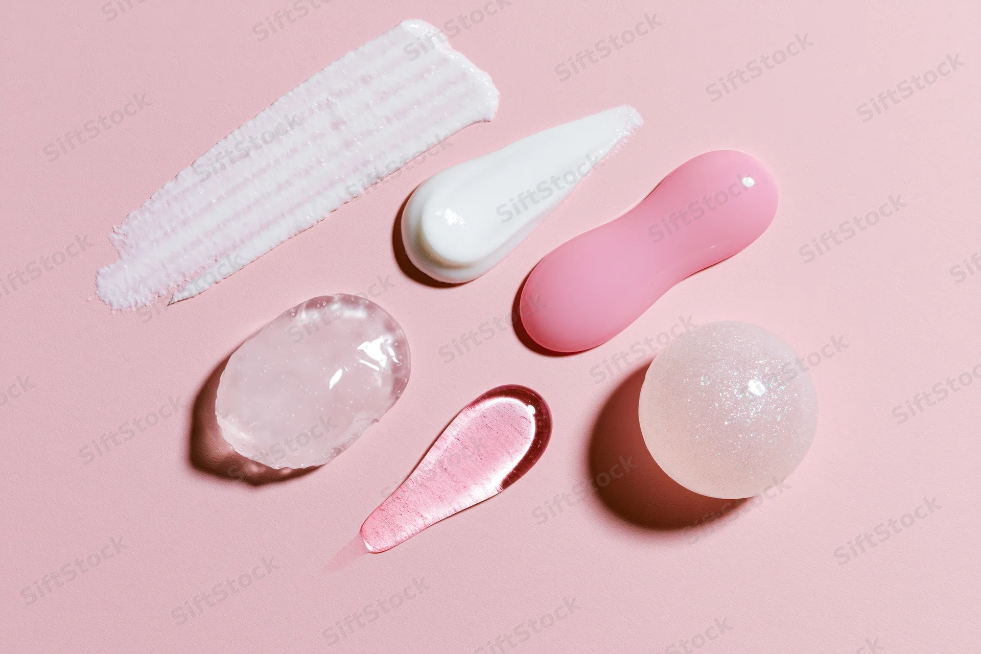Flat lay of skincare product swatches and dollops on a pale pink background