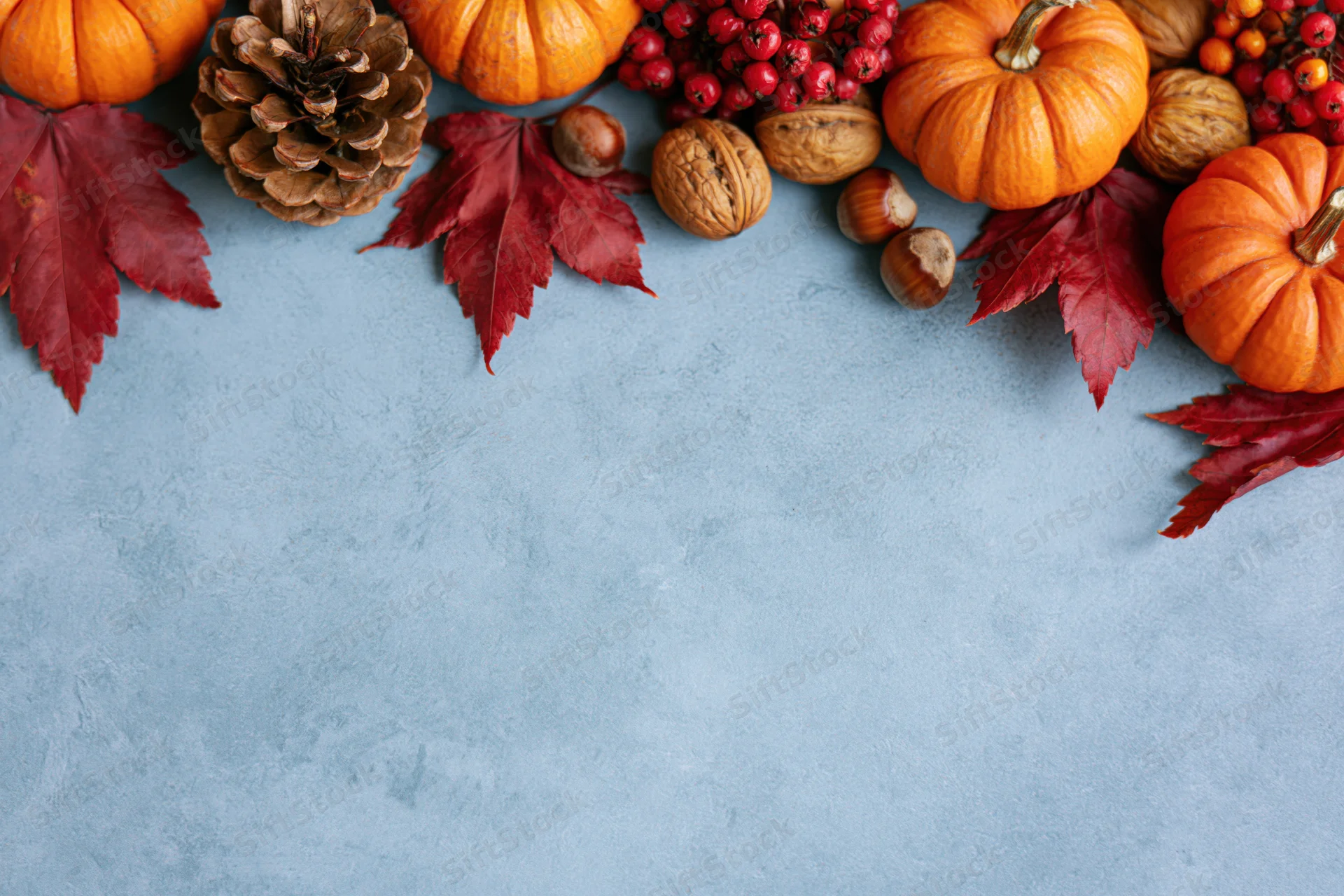 Small orange pumpkins and red maple leaves arranged in a border along the top of a blue textured surface with copyspace below