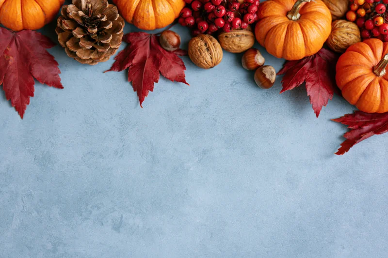 Small orange pumpkins and red maple leaves arranged in a border along the top of a blue textured surface with copyspace below