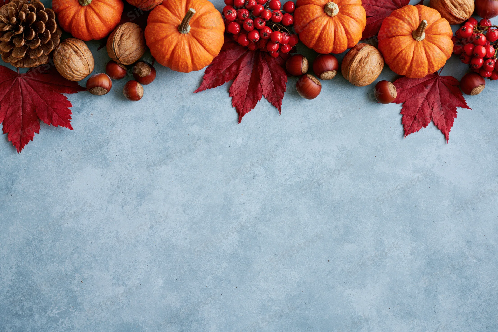 Small orange pumpkins and red maple leaves arranged in a border along the top of a gray textured surface with copyspace below