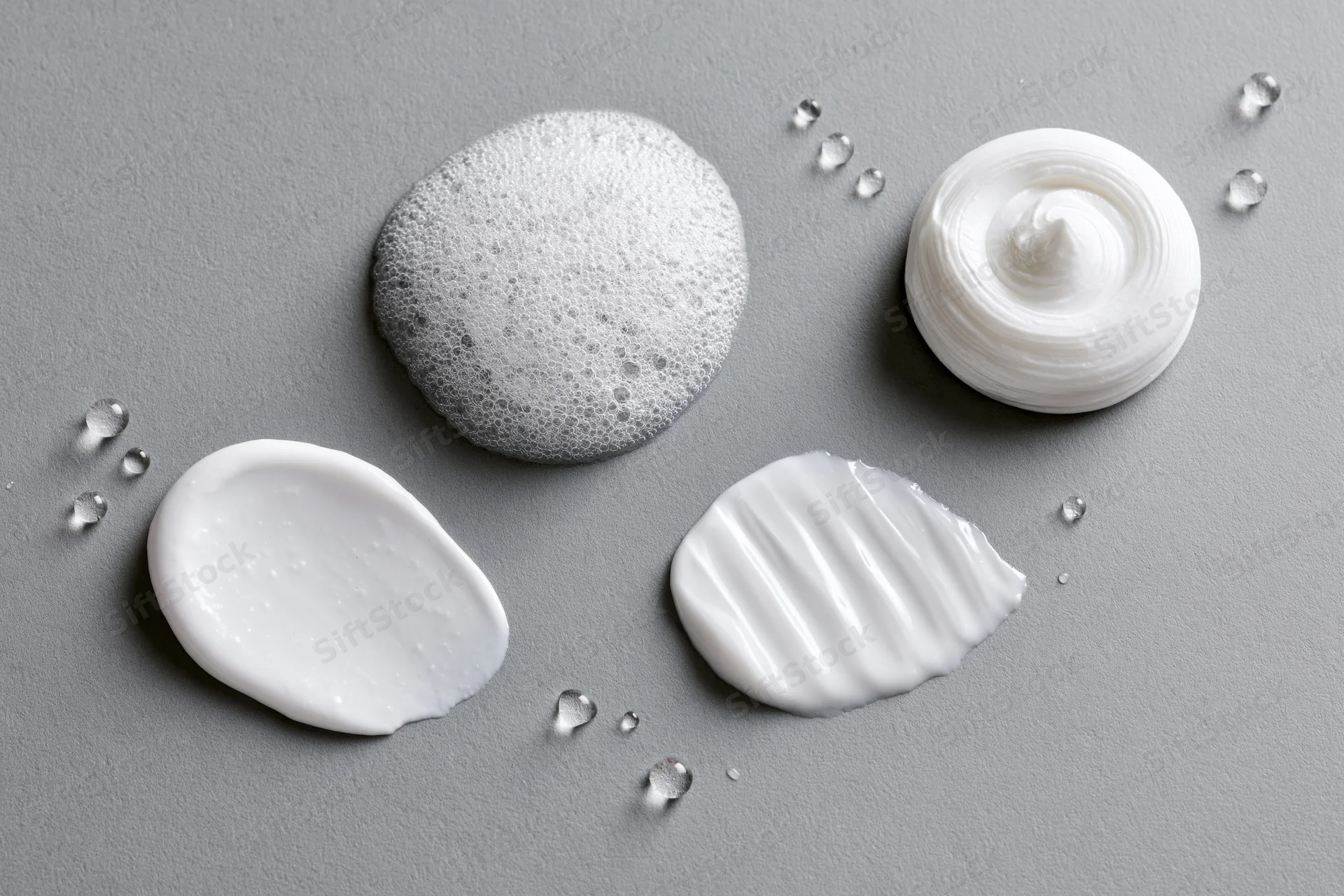 Four skincare product textures swatched on a smooth gray surface in flat lay arrangement
