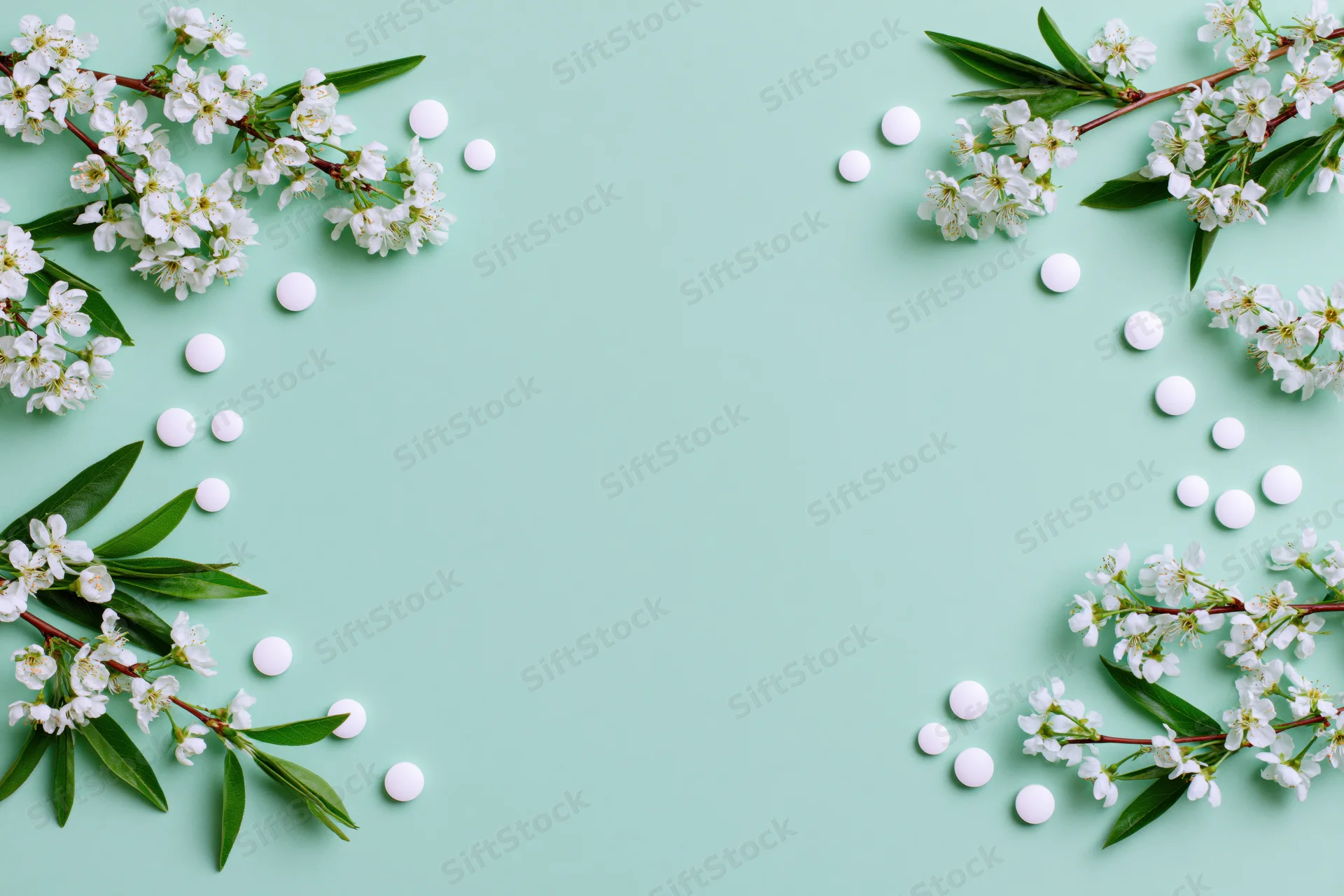 White blossoms and small white pills arranged on mint green surface in flat lay with copyspace