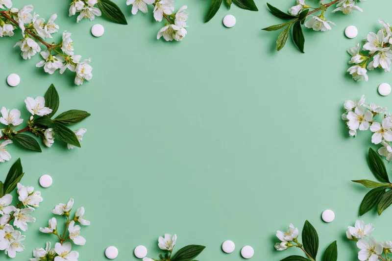 White blossoms and small white pills arranged in a frame on a mint green background