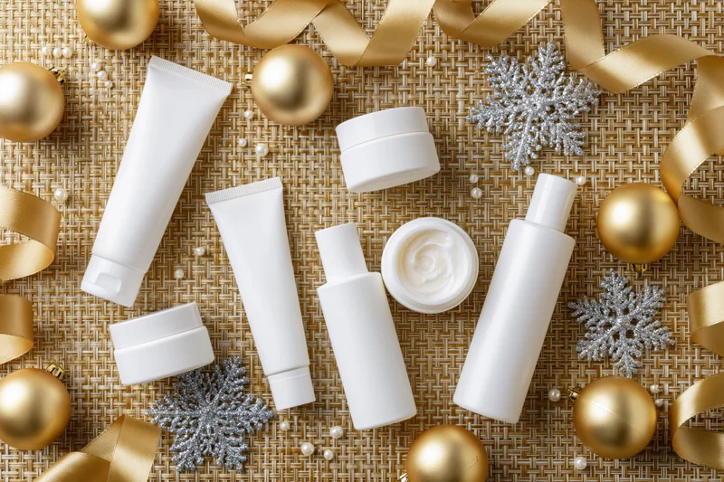 White skincare products arranged with gold ornaments and ribbons on woven background
