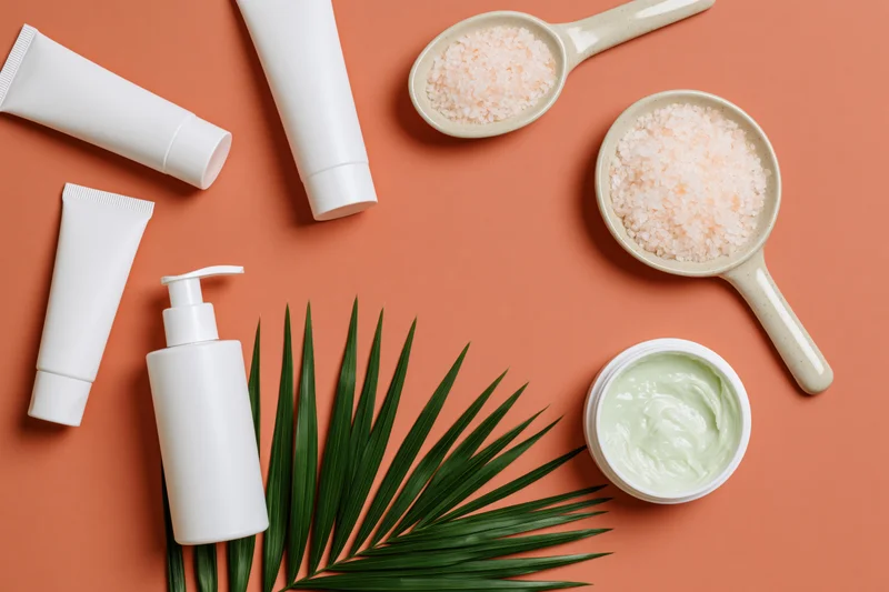 White unlabeled skincare tubes and pump bottle with salt and palm leaf on orange background